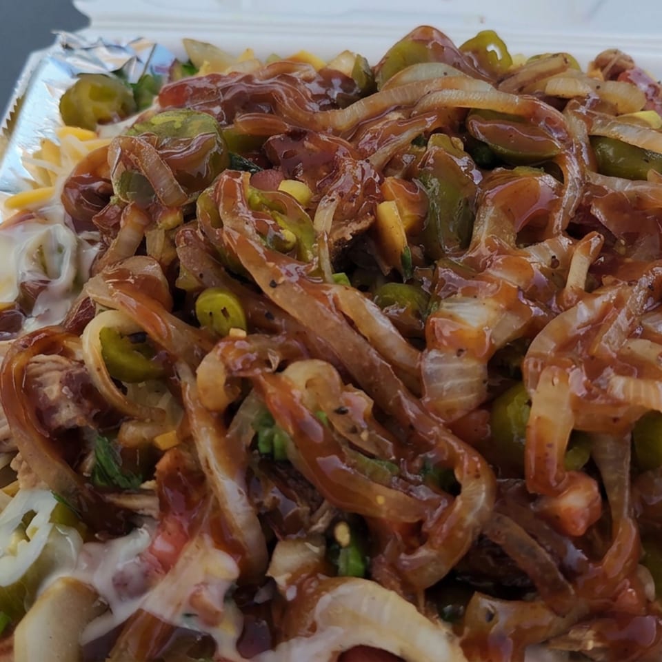 Loaded takeout platter topped with grilled onions, green peppers, barbecue sauce, shredded meat, cheese, pickles, and fresh salsa.